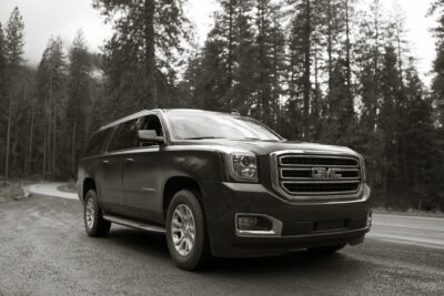 Black and white image of a GMC Yukon XL parked on a winding forest road.